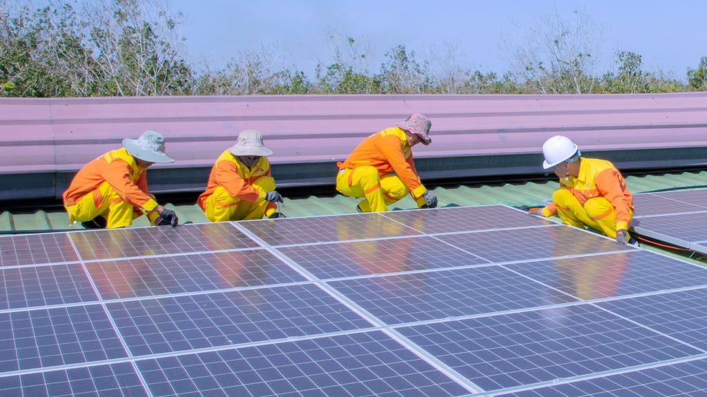 Four workers in orange and yellow safety suits installing solar panels on a roof